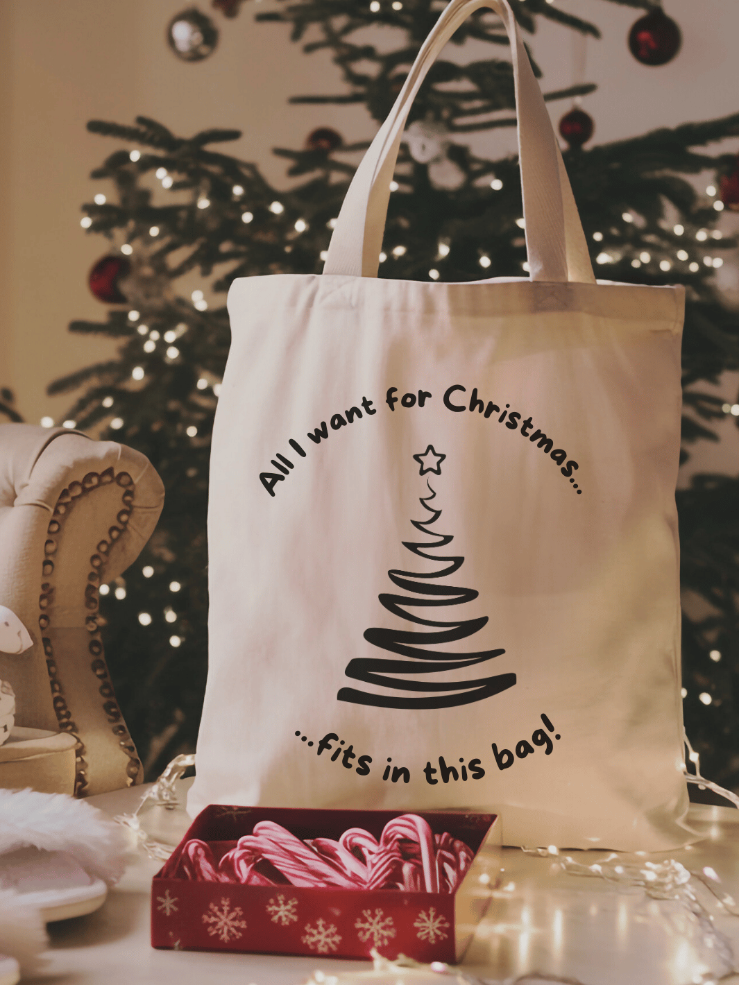 Eine naturfarbene Bio-Baumwolltragetasche, bzw. ein Einkaufsbeutel mit dem Motiv gezeichneter Weihnachtsbaum und dem Spruch: All i want for christmas fits in this bag steht vor einem Weihnachtsbaum mit Zuckerstangen davor