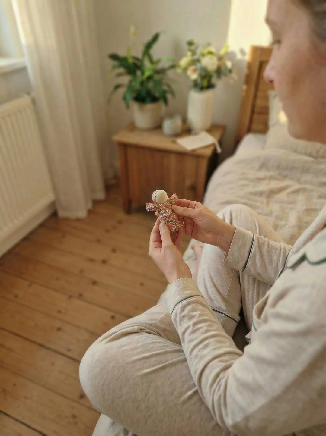 Frau hält ihr handgemachtes Sorgenpüppchen aus Baumwolle als symbolischer Mutmacher für innere Ruhe auf dem Bett in den Händen. Achtsame Geschenke für Frauen bei Alles auf Anfang in Bedburg, NRW